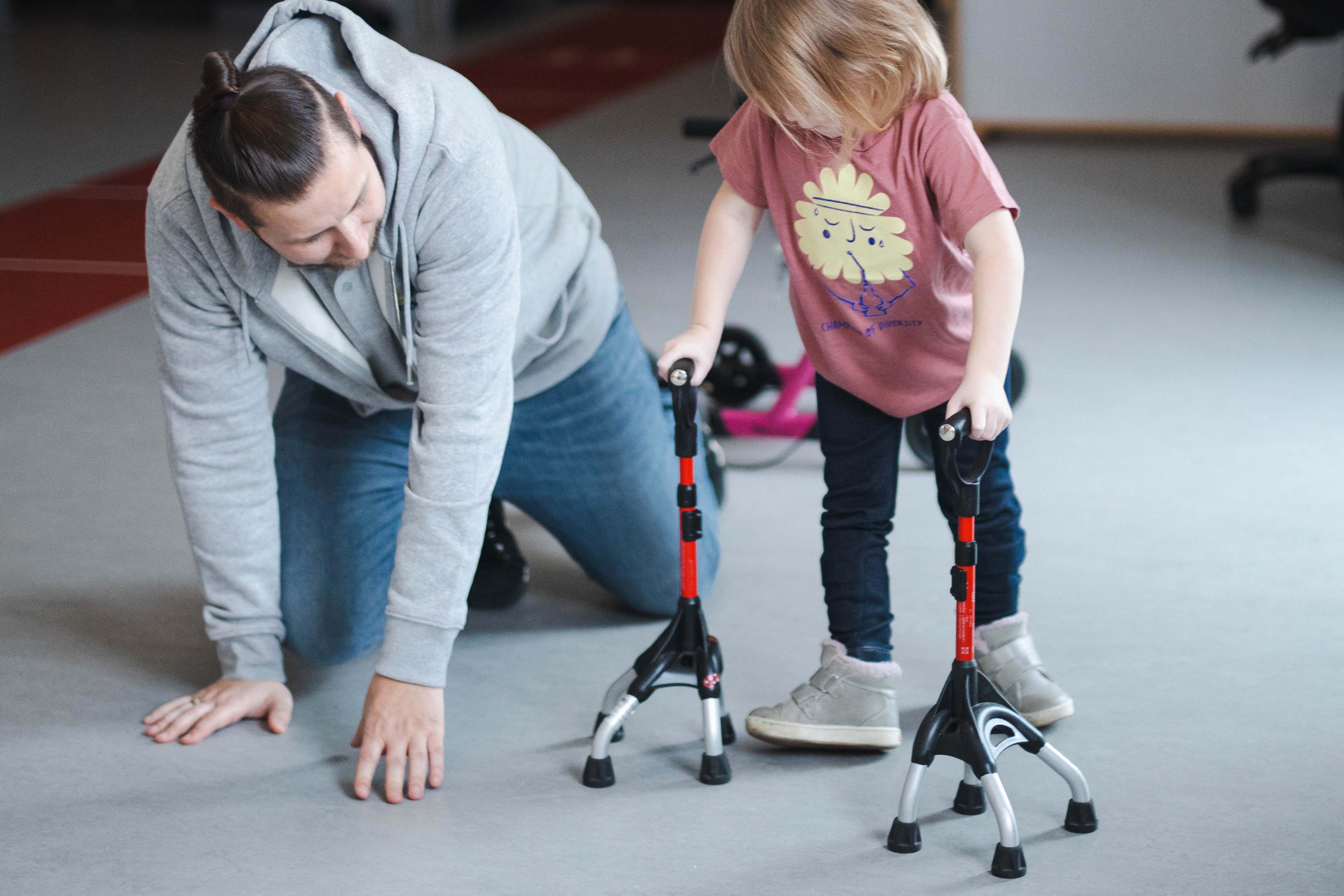 Tobias von Hodey Kids &uuml;bt mit einem kleinen M&auml;dchen das Fortbewegen mit Gehhilfen.